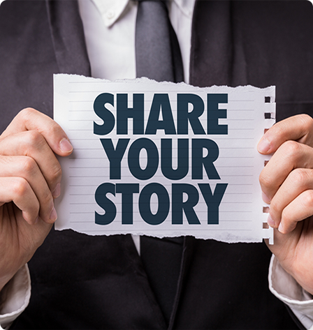 Man in suit holding a piece of paper with "Share Your Story" written on it in block letters.