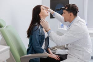 Handsome clever doctor wearing clean smock and rubber gloves putting his fingers on the forehead of his visitor while sitting in semi position - Deviated Septum