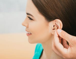 Young patient with Intra-ear hearing aid, close-up on female ear. The hearing solution, audiologist inserting hearing aid