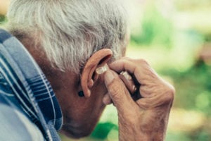 elderly man inserting his hearing aid into his ear.