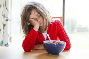 tired child sleeps at the breakfast table with a cereal in front of her