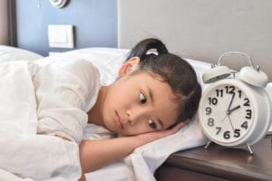 Asian girl child in bed do not sleep suffering insomnia (sleeping disorder) at night in bedroom next to an alarm clock