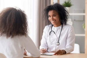 Smiling african american female doctor talking to teen patient making notes in clipboard listening to black kid school teenage girl tell complaints fill form at medical clinic checkup appointment.