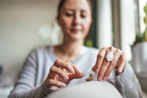 A woman holding her hearing aid to assist her with her hearing loss issues.