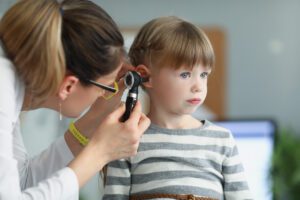 Doctor looking at ear of little girl using otoscope in clinic