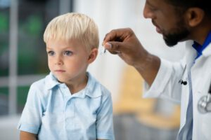 A cute baby receiving a hearing aid from a male Hearing loss specialist
