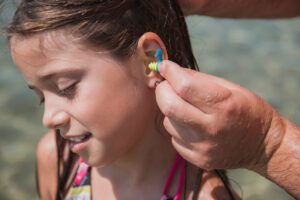 Image of a hand placing a protective water-resistant ear plug into a young girl's ear to help prevent a swimmer's ear infection.