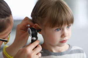 A female ENT doctor examines a little girl's ear with an otoscope in the clinic for an ear infection.