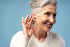 A smiling, happy senior woman with gray hair wearing a hearing aid due to hearing loss in one ear.
