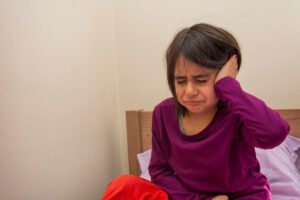 A primary school age girl sitting on her bed with earache.