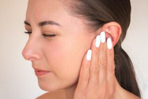 A close-up photo of a young Caucasian brunette woman experiencing acute ear pain.