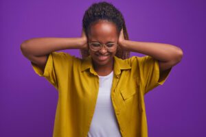 A young African woman is covering her ears due to pain and discomfort caused by ears rings.