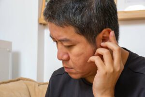 A middle-aged man is suffering from ear pain due to hearing loss at home.