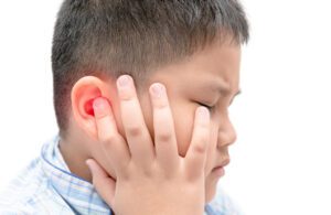 A boy holds his ear in pain from an ear infection.