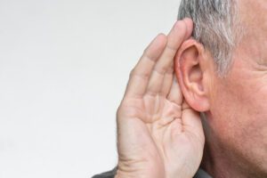 Elderly man with symptom of hearing loss in one ear with hand gesture to listen.