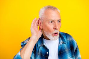 Senior man with hearing loss symptoms is cupping his ear and listening with a surprised face.